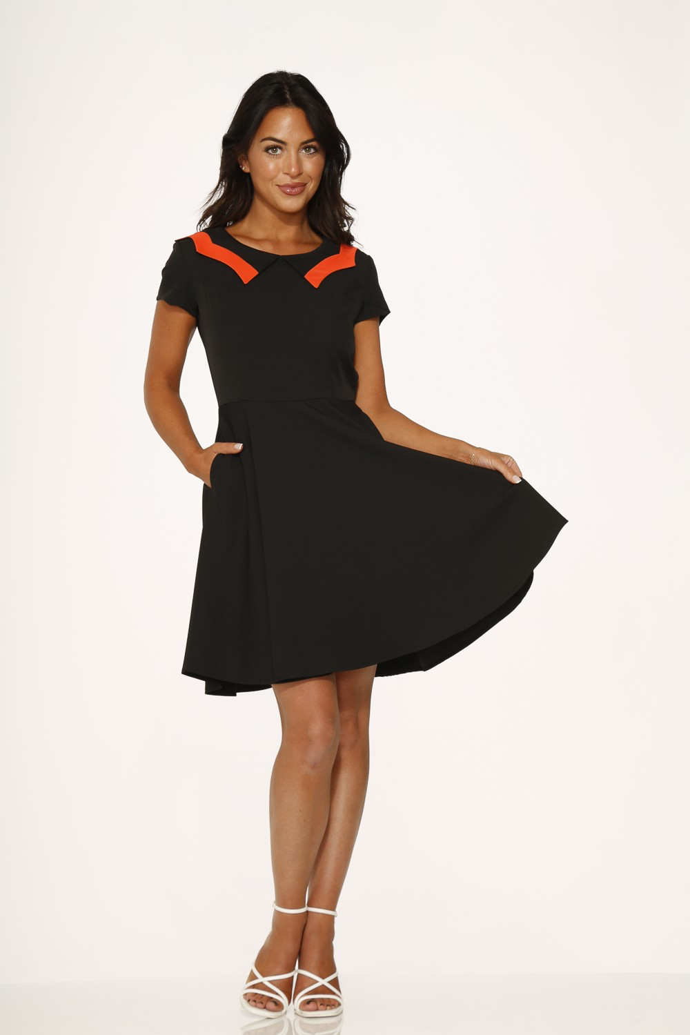 Model wearing a black short sleeve swing dress with an orange scalloped collar and pockets.