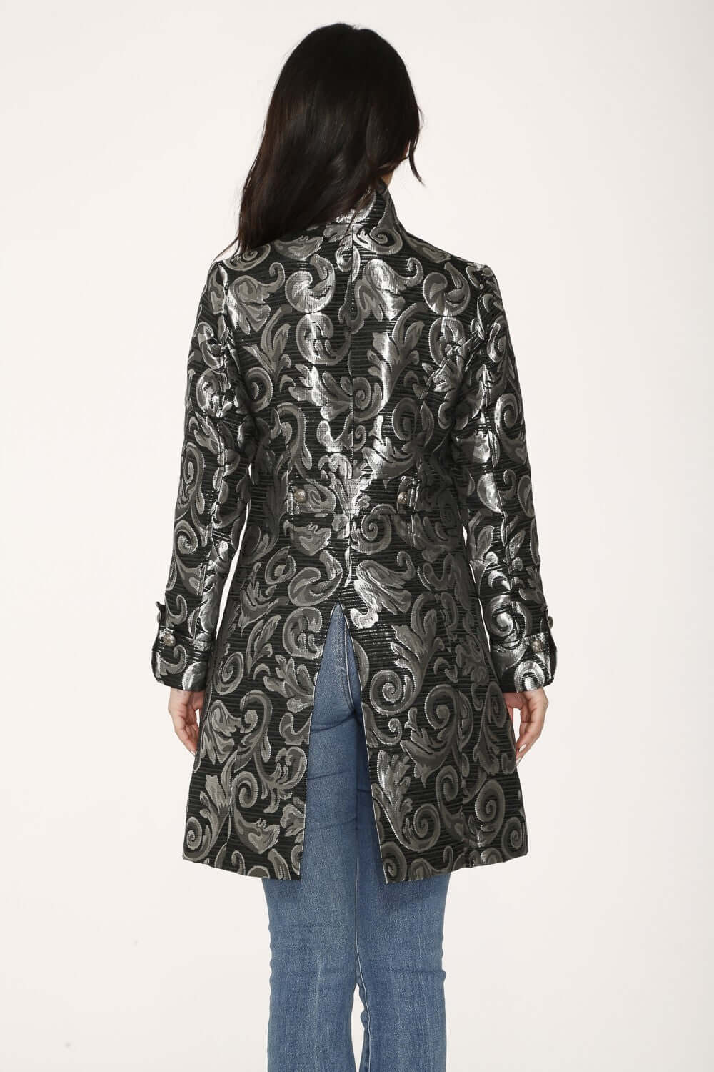 Back view of a woman wearing a silver brocade women's coat with a structured silhouette and metallic scroll design.