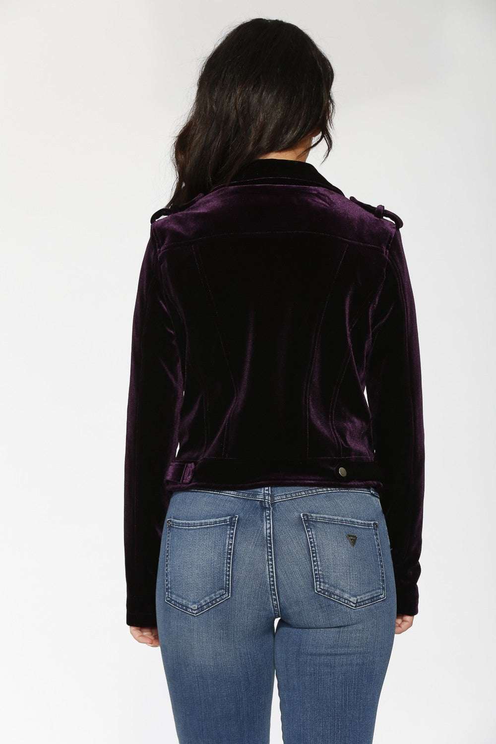 Person wearing a dark purple velvet jacket and blue jeans on a white background