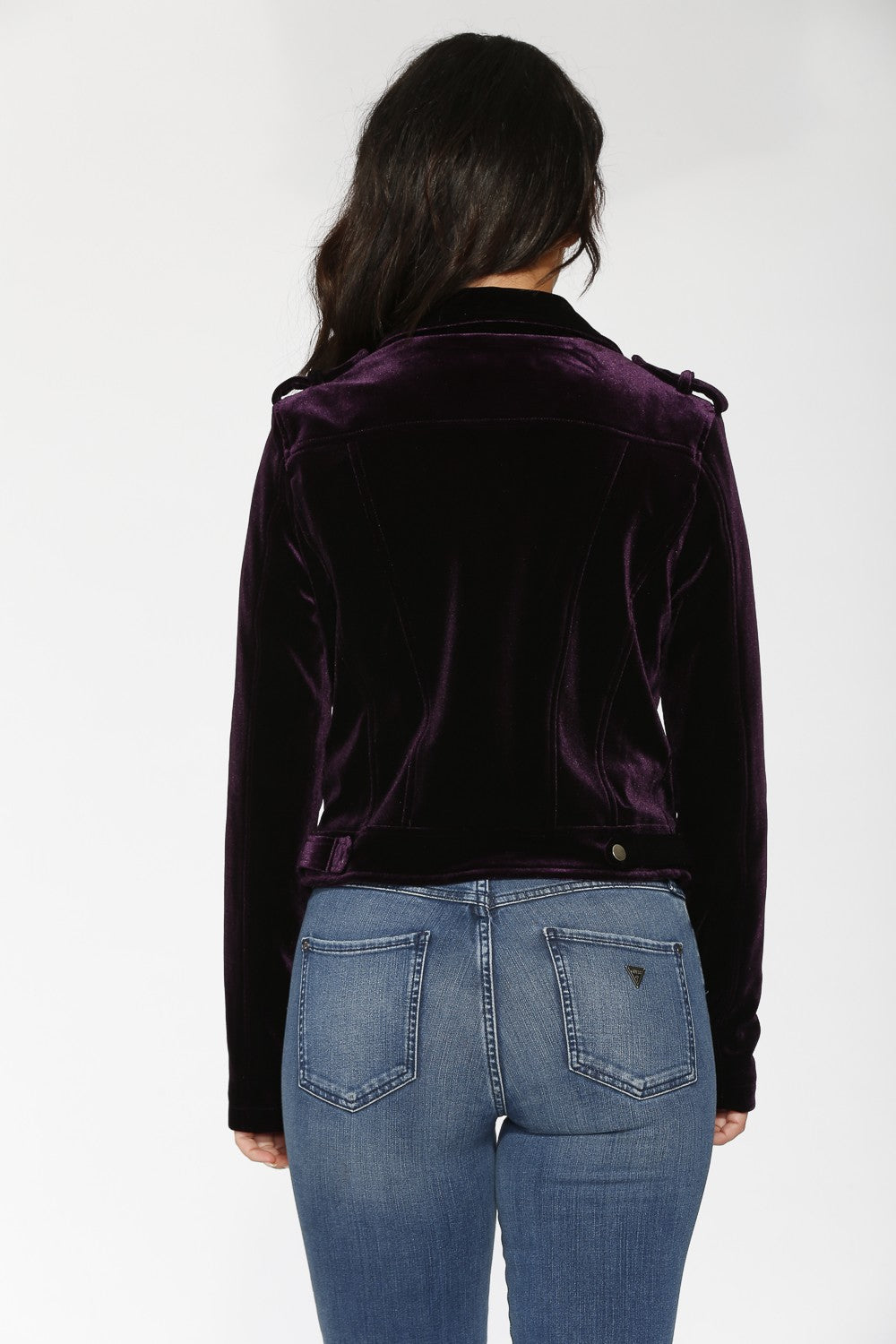 Person wearing a dark purple velvet jacket and blue jeans on a white background