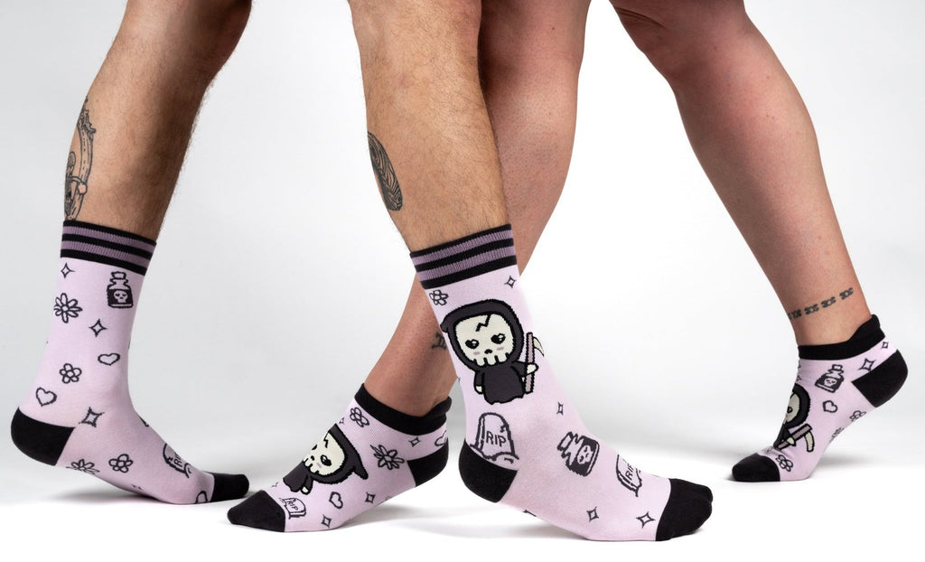 Pastel Goth Grim Reaper Ankle Socks featured on two pairs of feet with playful skull designs.