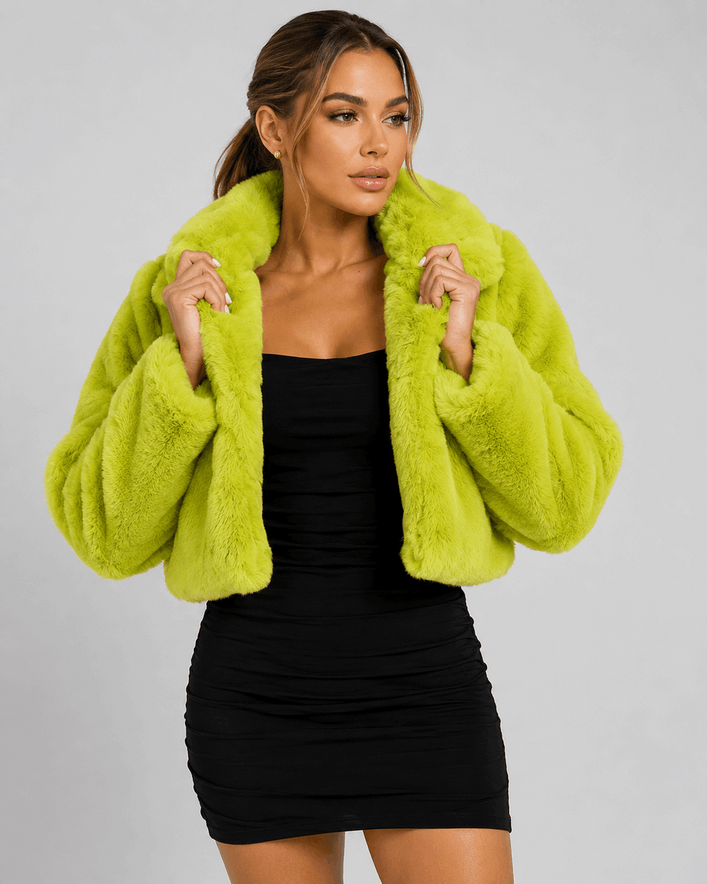 Woman wearing a bright green faux fur jacket over a black dress on a gray background