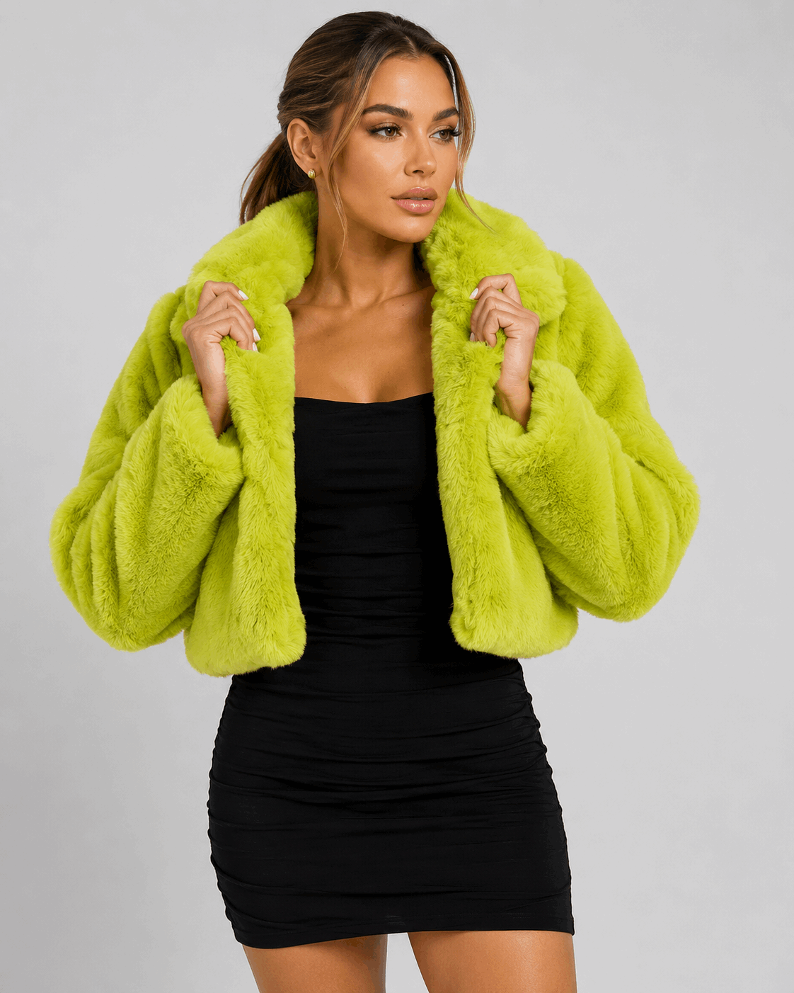 Woman wearing a bright green faux fur jacket over a black dress on a gray background