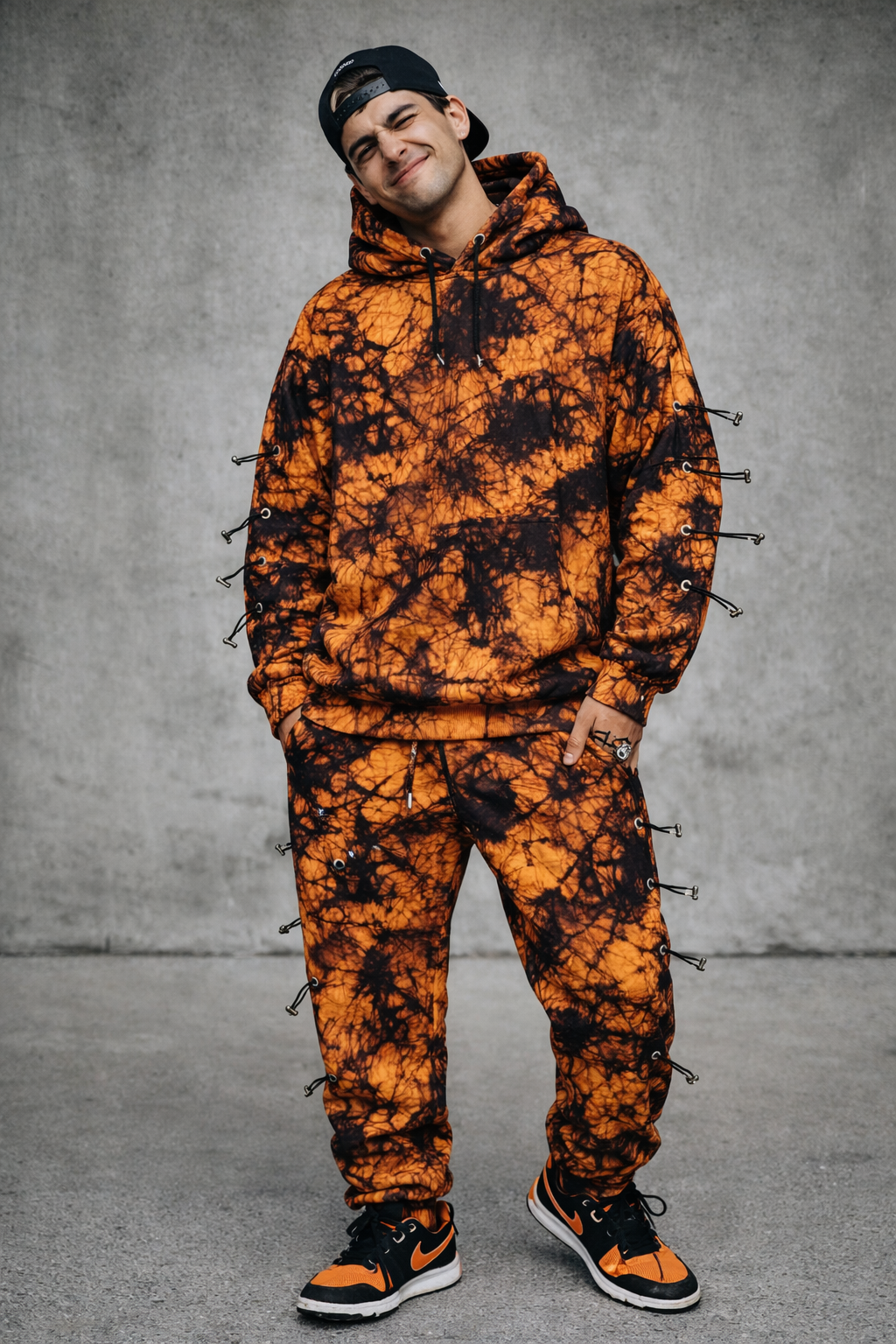 Tie-dye hoodie and sweatpant set in orange and black with decorative toggle hardware on sleeves and pants.