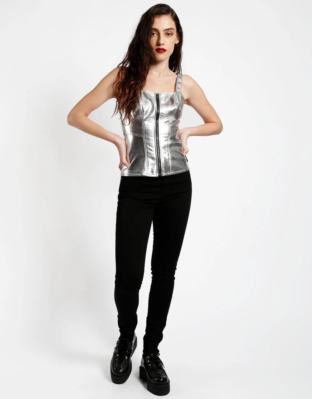 Model wearing Tripp NYC metallic faux leather corset top with zip front, paired with black pants and platform shoes.