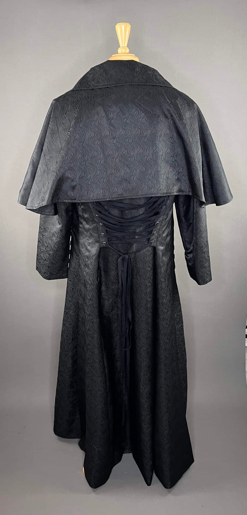 Swirling brocade cape coat showcasing dramatic cape-style silhouette and richly textured fabric.
